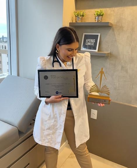 Dra. Mariana Damasio Waschevicz sorrindo ao segurar um certificado e um troféu em sua clínica